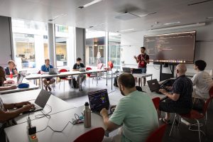 People attending a workshop sitting in front of their laptops. A teacher is explaining something.
